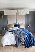 Different coloured blankets on double bed with canopy and upholstered headboards on grey wooden wall in rustic bedroom