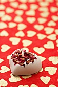 Bath bomb with rose petals on a red background patterned with hearts