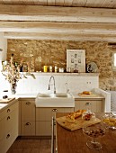 Storage jars of groceries on kitchen island in front of counter with tiled splashback on stone wall in rustic setting