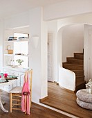 Open living room with eating area in front of a separating wall and a view through a wide doorway of a winding, wooden staircase