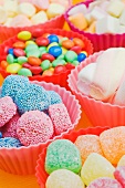 An assortment of sweets: jelly sweets, chocolate beans and marshmallows in colourful plastic bowls