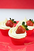 Three cupcakes with vanilla icing and fresh strawberries