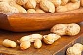 Peanuts, whole and shelled, in and in front of a wooden bowl
