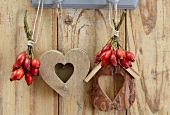 Bunches of rosehips and wooden hearts hanging on hooks on wooden wall
