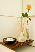 Soap, fragrance sticks and cut rose on wooden slatted rack over shallow washbasin