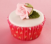 A cupcake with white glaze and a sugar rose