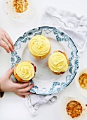 Hands reaching towards cupcakes which are on a plate