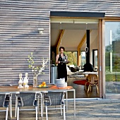 Meal on sunny terrace - view through open door of woman in living room carrying tray of glasses