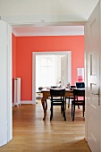 View through open double doors of table and dark wood chairs in front of salmon pink wall