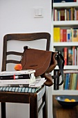 Apricot on stack of books and brown handbag on antique chair against wall next to open doorway showing view of bookcase beyond
