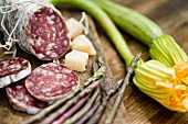 A salami, partly sliced, and cubes of parmesan, with green asparagus and courgette flowers
