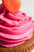A cupcake topped with pink icing and a red sugar heart (close-up)