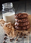 Double Chocolate Coffee Cookies Stacked on Burlap on a Table with a Glass of Milk