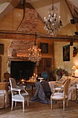 Rustic country house - living room - chandelier above Rococo-style armchairs and simple wooden table draped with tablecloth in front of open fire
