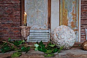 Blätterzweig neben Steinkugel mit Pflanzenmuster und Kerzenständer mit brennender Kerze auf Tisch vor Holztür mit Paneelen und abblätternder Farbe