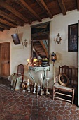 Rustikaler Hausflur eines französischen Landgutes mit antiken Kerzenleuchtern auf dem Boden vor Rokoko-Konsolentisch