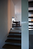 View from staircase of simple dining table and chairs below pendant lamp next to window
