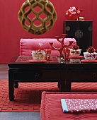Asiatischer Teetisch in Schwarz mit Schalengedecken auf rotem Teppichläufer vor roter Wand