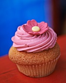 A cupcake topped with pink icing and a flower decoration