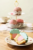 A cupcake with a strawberry buttercream filling and topped with turquoise icing, with a tiered cake stand in the background