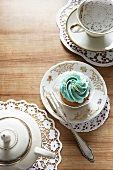 A teaset and a cupcake topped with turquoise icing