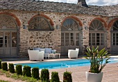 Topiary cypresses in front of pool and terrace with white seating in courtyard of Mediterranean residential complex
