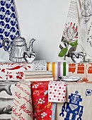 Colourful tea towels hanging on wall and lying on table