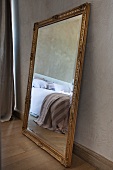 Mirror with traditional gilt frame on parquet floor leaning against wall