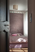 Blick durch halboffene Tür auf Doppelbett vor Raumteiler in pastellfarbenem Schlafzimmer
