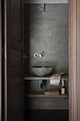 View through open door of simple washbasin on wooden counter against wall painted using trowelling technique