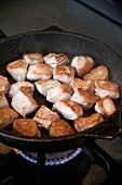 Chunks of pork being fried in an iron pan