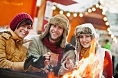 Two women and one man warming themselves around fire at Christmas market