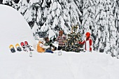 Junge Leute sitzen um einen Christbaum im Schnee
