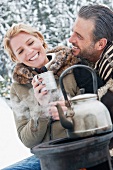 Couple sitting by camping stove in snow drinking tee