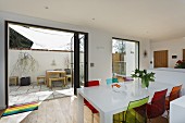 Farbige Kunststoff Stühle an weißem Esstisch vor offenen Terrassentüren und Blick auf Innenhof