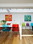 Colourful plastic chairs at white dining table opposite modern artworks on wall