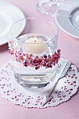Floating candle in glass decorated with confetti on doily
