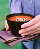 A hand holding a bowl of spicy tomato soup