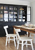 White, retro kitchen chairs at rustic wooden table and display cabinet made from black metal