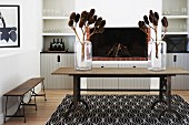 Branches of cones in glass vases on rustic wooden table in front of open fireplace in modern interior