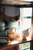 White and pastel turquoise coffee service on simple wooden shelf behind reflective glass