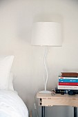 Bedside lamp with base shaped like stylised tree and stack of books on modern table with drawer
