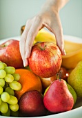 Frauenhand nimmt einen Apfel vom Obstteller