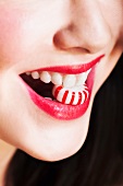 Close up of woman's mouths with red lipstick holding striped candy