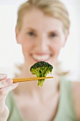 Woman holding broccoli in chopsticks