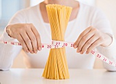 Close up of woman's hands measuring pasta with tape measure