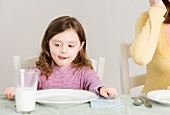 Mädchen sitzt am Tisch mit leerem Teller und einem Glas Milch