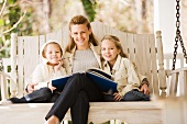 Mother reading to daughters on porch swing