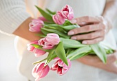 Frau hält Blumenstrauss mit rosafarbenen Tulpen