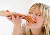 Junge Frau beisst genussvoll in ein grosses Stück Pizza